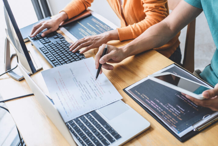 Two professional programmer cooperating and working on web site project in a software developing on desktop computer at company, codes and typing data code, Programming with HTML, PHP and javascript.