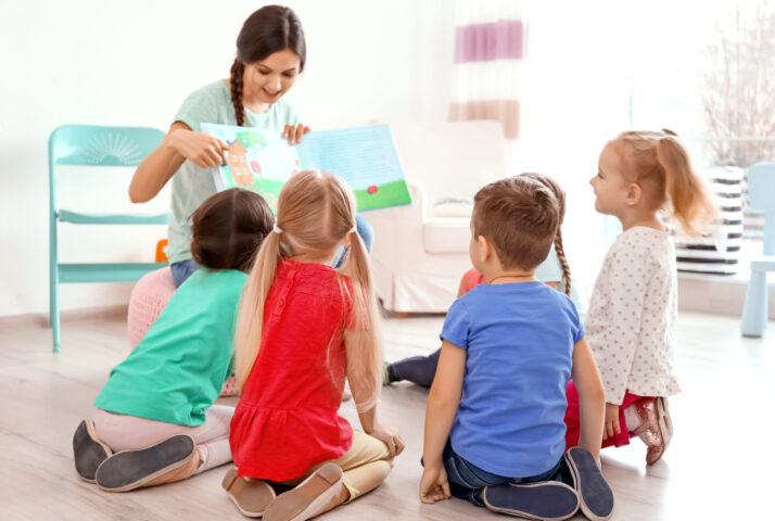 Female teacher reading book to little children in kindergarten
