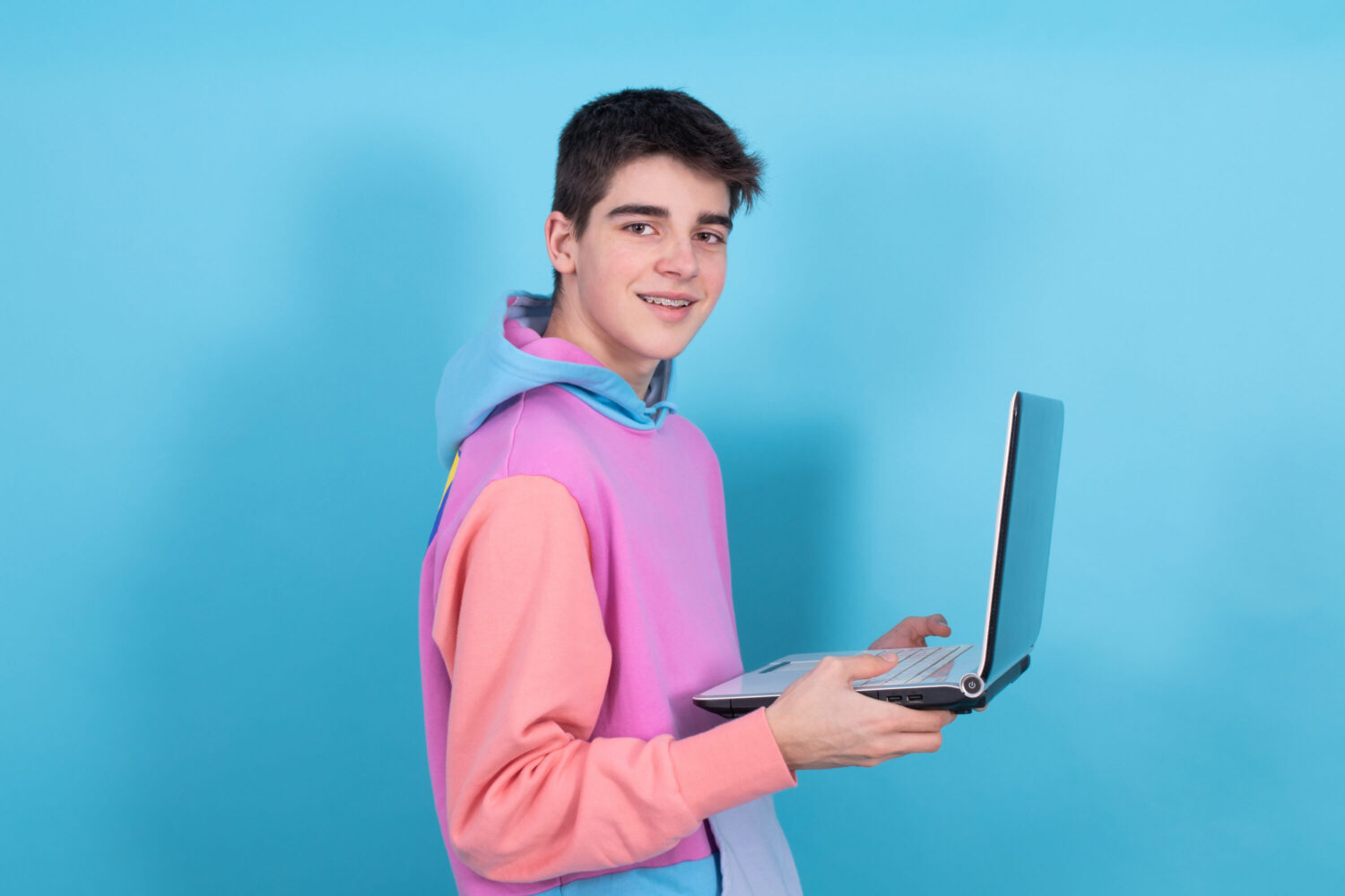 young teenage man or student with laptop isolated on blue background
